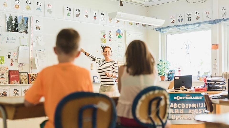 Kvinnlig lärare pekar på whiteboard-tavla när hon undervisar sina elever i ett klassrum