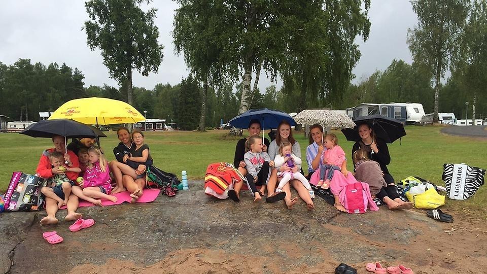 Regn eller sol det spelar ingen roll, på stranden vid Duse Udde sitter ett stort glatt gäng med barn och vuxna under paraplyer