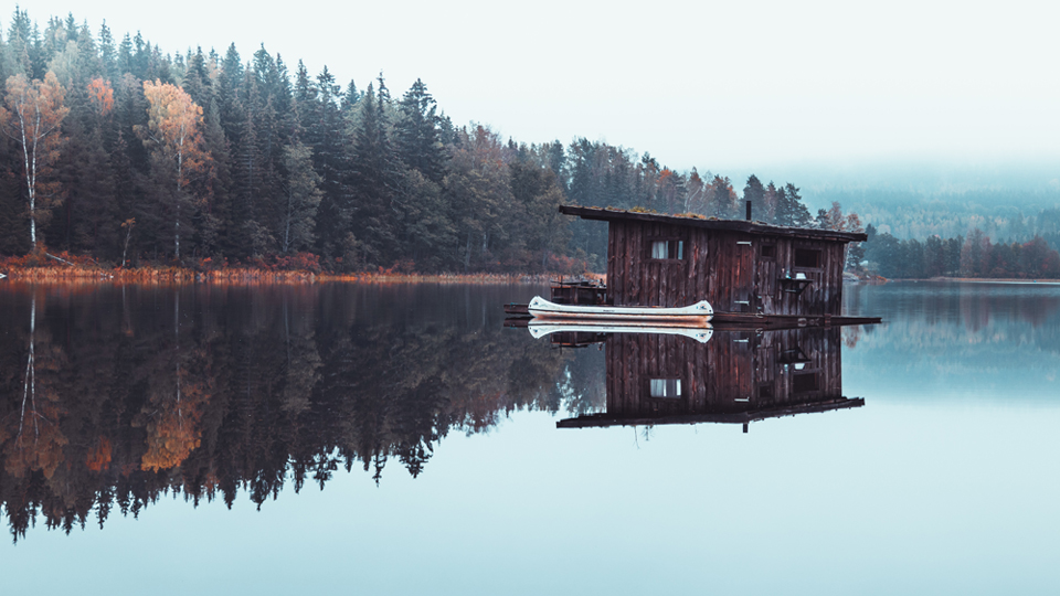 Fotot är tagen i Naturbyn utöver den spegelblanka sjön där den timrade husbåten ligger. Foto av Christan Gård