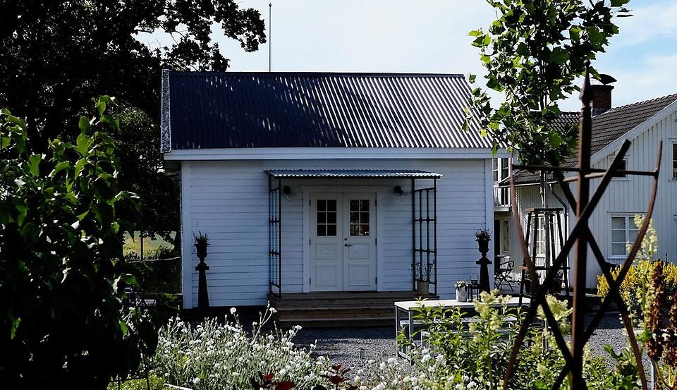 Ett vitt hus med ett svart tak mitt i en trädgård. 